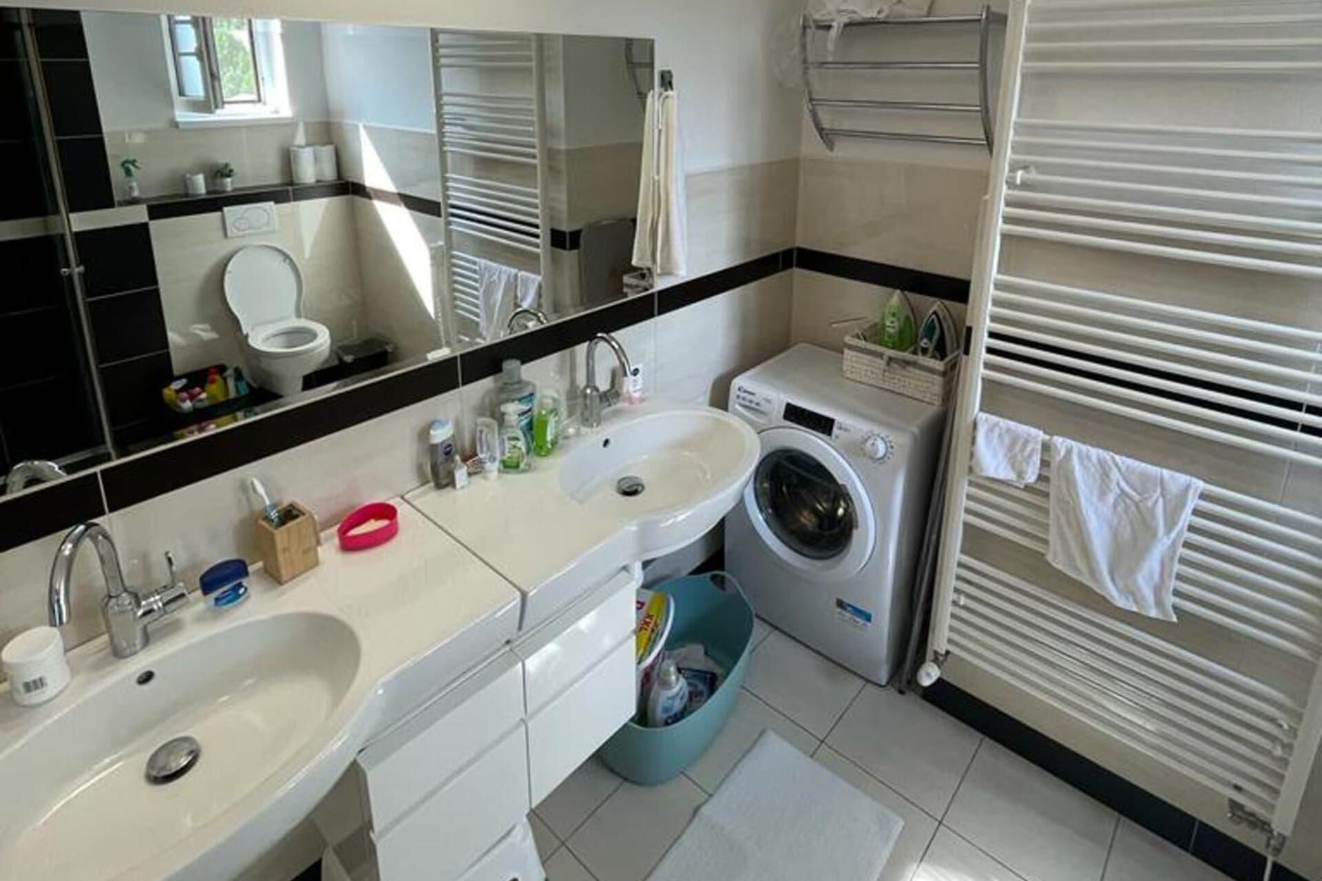 A bathroom with a sink, mirror, toilet, and a washing machine.