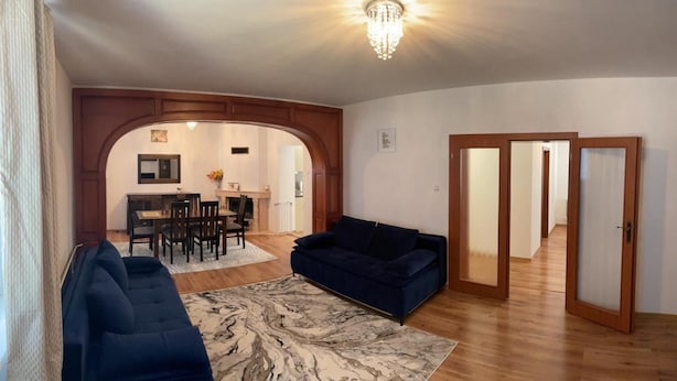 Un vaste espace de vie comprenant un canapé bleu foncé, un tapis à motifs de marbre et une table à manger en bois avec des chaises.