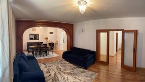 Amplia sala de estar con un sofá azul oscuro, un tapete con diseño de mármol y una mesa de comedor de madera con sillas.