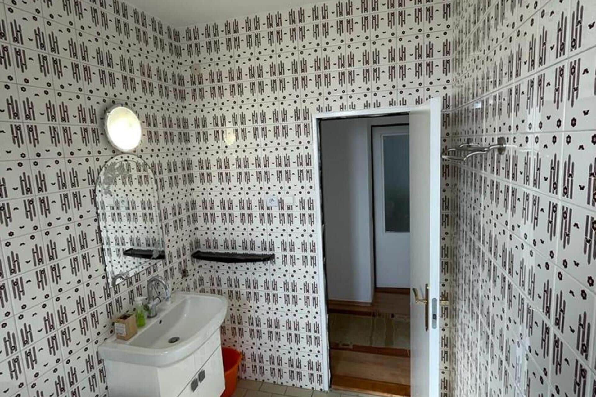A bathroom with a sink, mirror, and patterned walls.