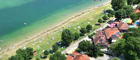An aerial view of a lakeside area with a beach, tents, and houses with solar panels.