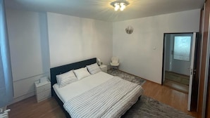 Une chambre à coucher comprenant un lit, une table de chevet, une lampe et une porte donnant sur une autre pièce.