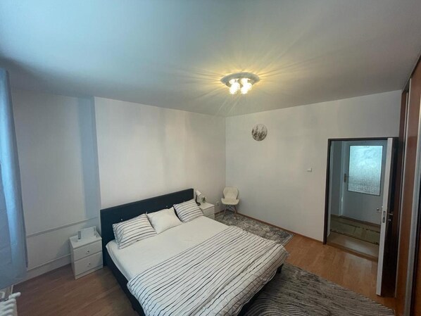 Une chambre à coucher comprenant un lit, une table de chevet, une lampe et une porte donnant sur une autre pièce.