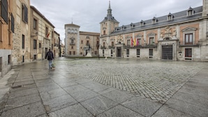 Un amplio patio con empedrado de piedra, edificios históricos de arquitectura clásica y una imponente torre de iglesia.