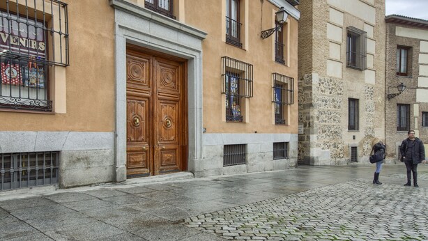 Un edificio con una puerta de madera grande y varias ventanas con barrotes de metal.