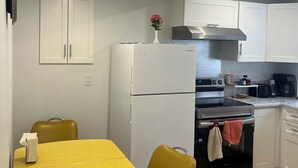 A compact kitchen with white cabinets, a refrigerator, an oven, and a dining table with yellow chairs. - Welcome to our home. We speak English and mandarin if needed. (Kamloops)