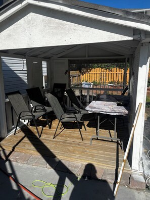 Un porche cubierto con una mesa y sillas, una terraza de madera y vistas a una cerca amarilla.