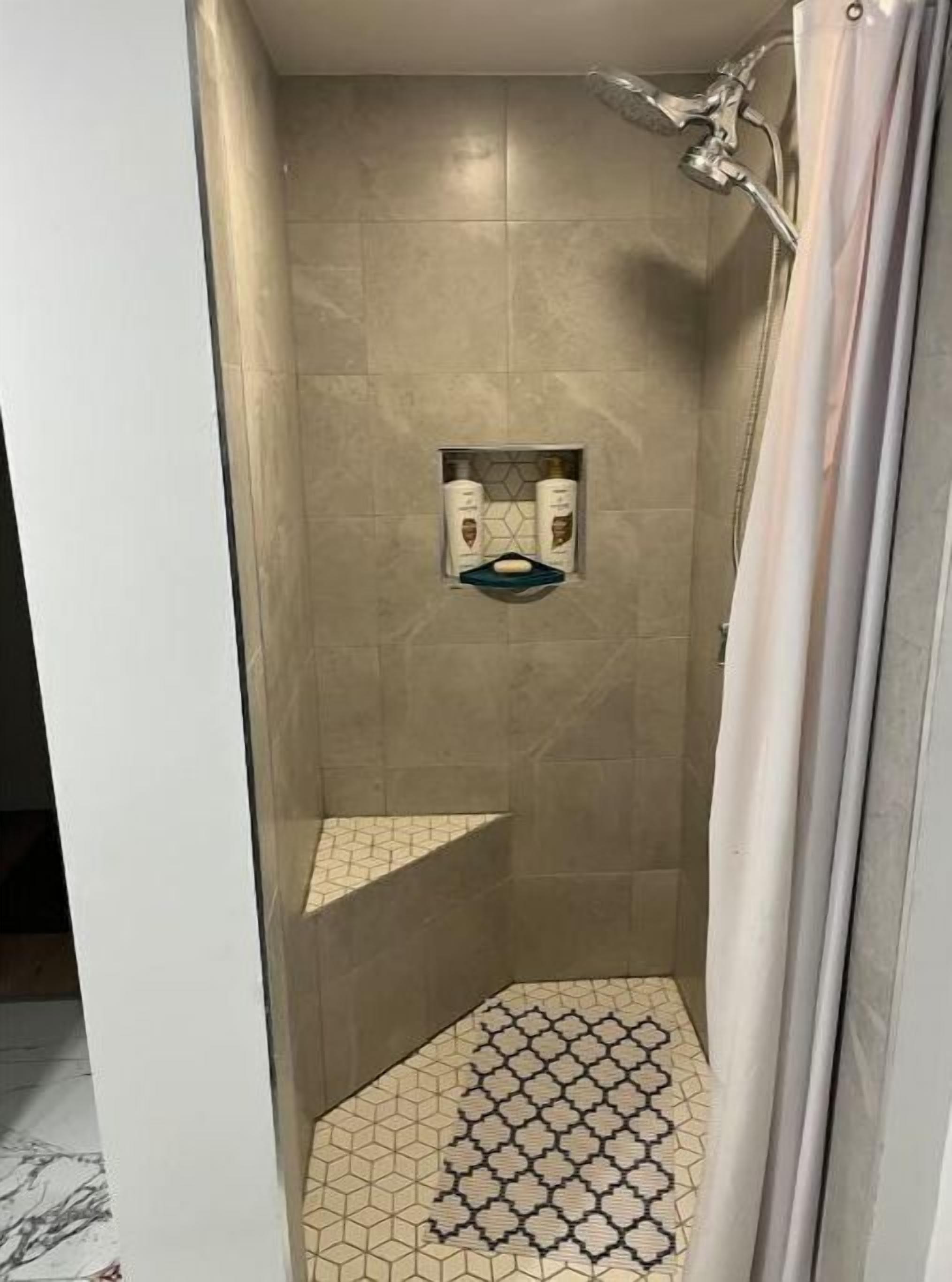 A shower with a tiled floor and a small shelf with toiletries.
