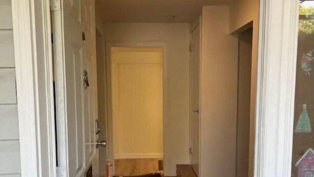 A hallway with a wooden floor, white walls, and a door at the end. - Welcome to our home. We speak English and mandarin if needed. (Kamloops)