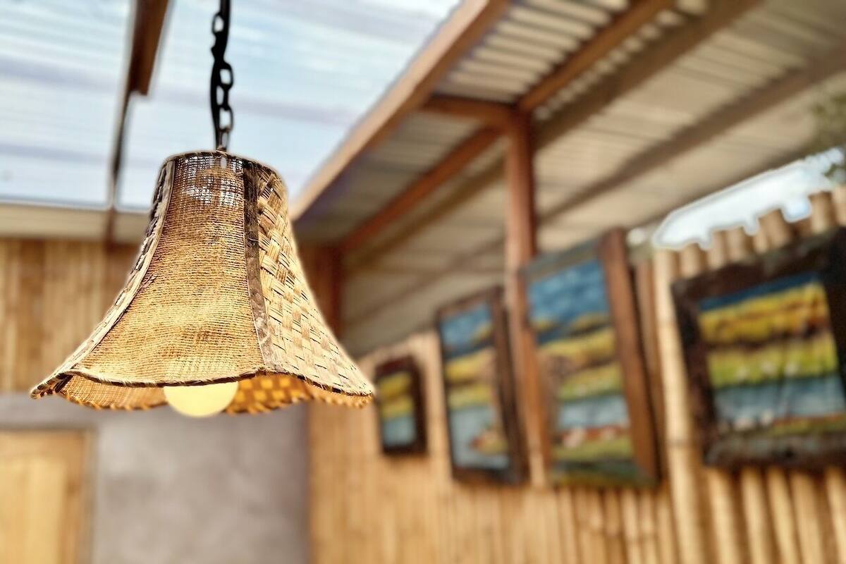 A hanging woven light fixture in a rustic setting with wooden walls and framed artwork.