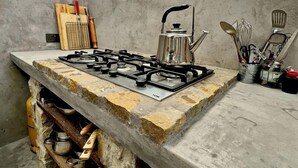 Cuina rústica amb fogó de gas, prestatges de fusta i finestra amb vista a vegetació.