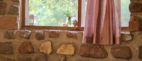 Una habitación rústica con pared de ladrillo, ventana con vistas a follaje y cama con manta a rayas.