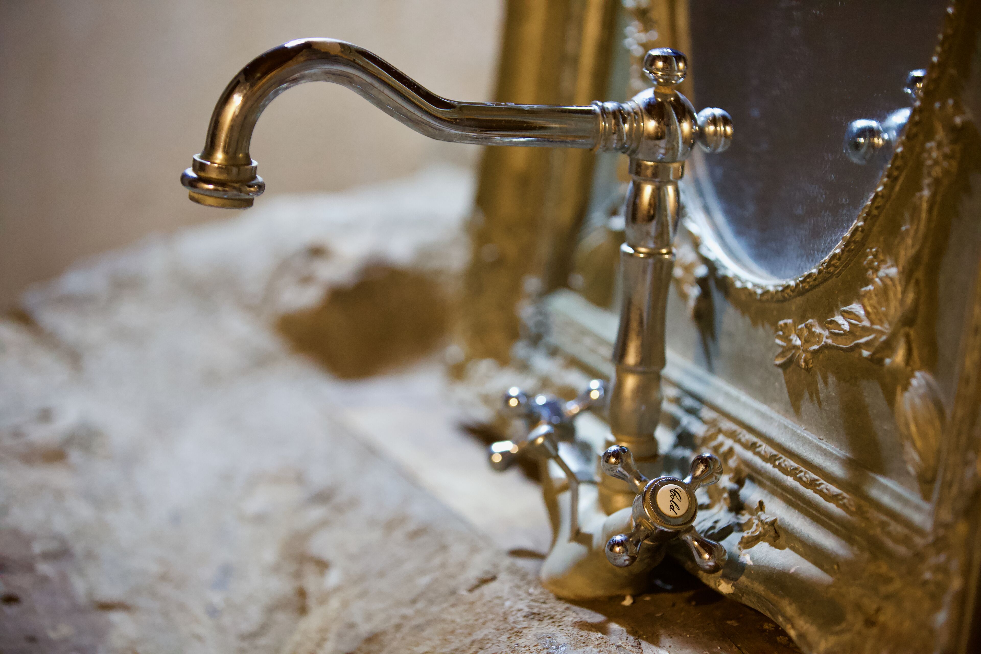 A close-up of a brass faucet with intricate design, attached to a vintage mirror frame.