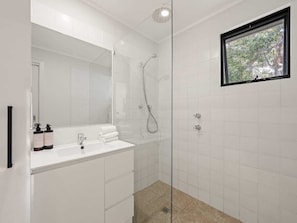 A modern bathroom with a glass shower enclosure, a white vanity with a mirror, and a window with a view of trees.