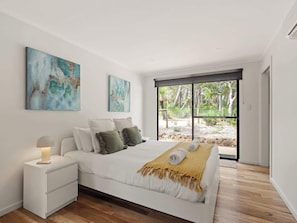 A modern bedroom with a large bed, a bedside table with a lamp, and two abstract paintings on the wall.