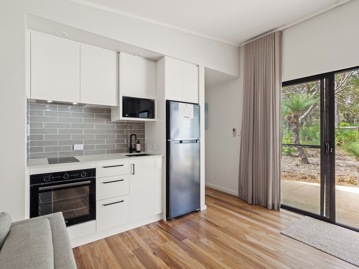 A modern kitchen with white cabinets, a stainless steel refrigerator, and a built-in oven.