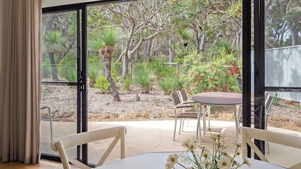 A room with a large sliding glass door leading to an outdoor patio with a table and chairs, surrounded by greenery and trees. - Wren Studio - Private One-Bedroom Studio Nestled in Bushland (Yallingup)