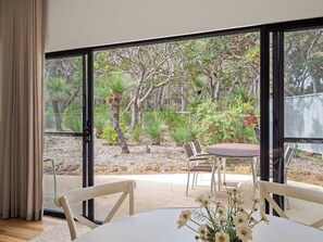 A room with a large sliding glass door leading to an outdoor patio with a table and chairs, surrounded by greenery and trees. - Private One-Bedroom Studio Nestled in Bushland (Yallingup)