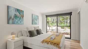 A modern bedroom with a large bed, a bedside table, and a view of the outdoors through a sliding door.