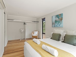 Ein modernes Schlafzimmer mit einem Bett, einem Sessel, einem Ventilator und einem Bild an der Wand.