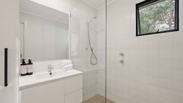 A modern bathroom with a glass shower enclosure, a white vanity with a mirror, and a window with a view of trees.