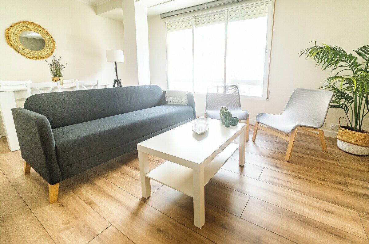 Una sala de estar con un sofá gris, una mesa de centro blanca, una silla y una planta en maceta.