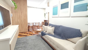 Ein modernes Wohnzimmer mit einer Couch, einem Couchtisch und einem Fernseher. Es gibt einen Essbereich mit Stühlen und einem Tisch.