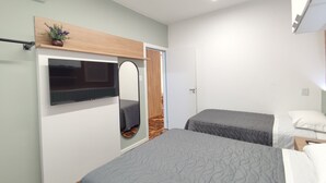 Ein modernes Schlafzimmer mit zwei Betten, einem Fernseher, einem Spiegel und einem Holzregal mit einer Pflanze.