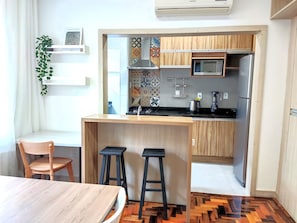 Une cuisine compacte dotée de meubles en bois, d’un four à micro-ondes, d’un réfrigérateur et d’un petit coin bar avec des tabourets.