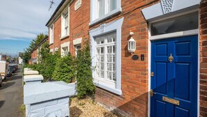 Une rangée de maisons mitoyennes avec une porte bleue, des volets blancs et une plaque d’immatriculation.