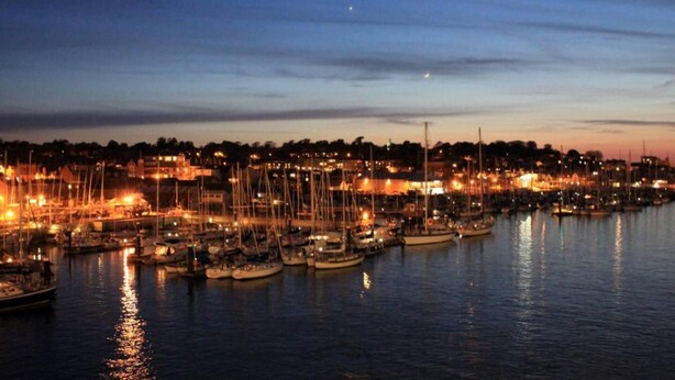 Un port de plaisance au crépuscule, avec des bateaux amarrés et les lumières de la ville en arrière-plan.