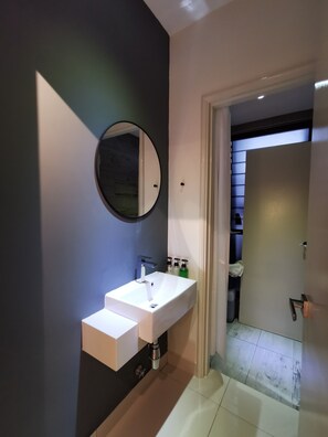 A modern bathroom with a white sink, a round mirror, and a door leading to a shower area.