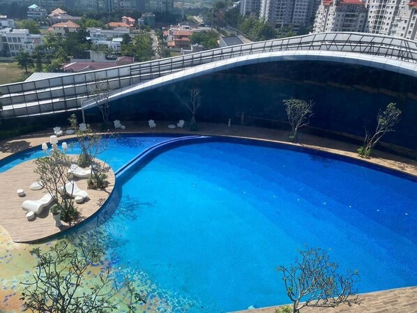 A swimming pool with a curved bridge, surrounded by trees and outdoor seating.