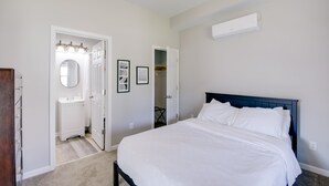 Un dormitorio con cama, pared blanca, ventilador de techo y aire acondicionado blanco.
