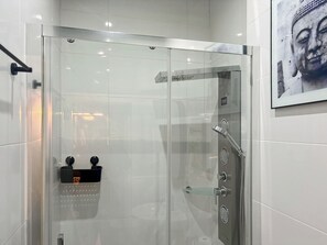 Une cabine de douche moderne dotée d’une porte en verre, d’un pommeau de douche à main et d’un panneau de commande fixé au mur.