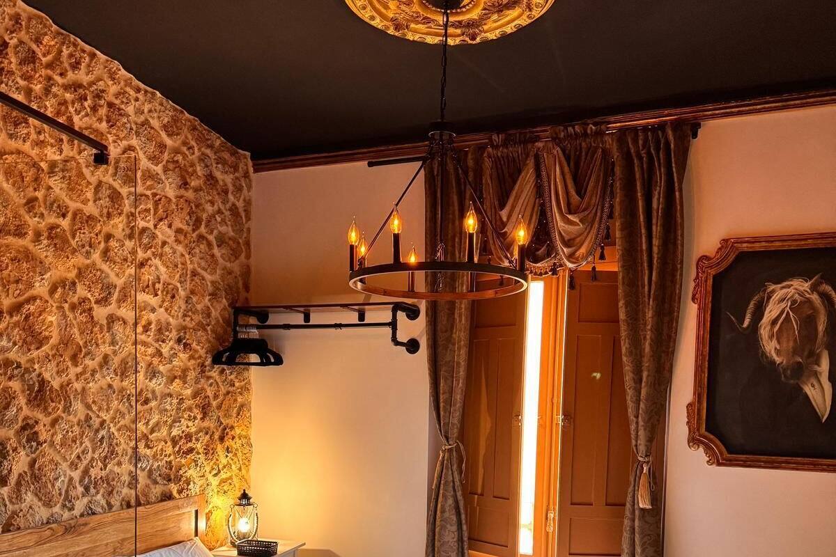 Un dormitorio con pared de piedra, una cama de madera, una araña y una cabeza de animal enmarcada en la pared.
