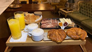 Bandeja de desayuno con cruasanes, jamón, queso y jugo en una habitación acogedora con pared de piedra y escalera.