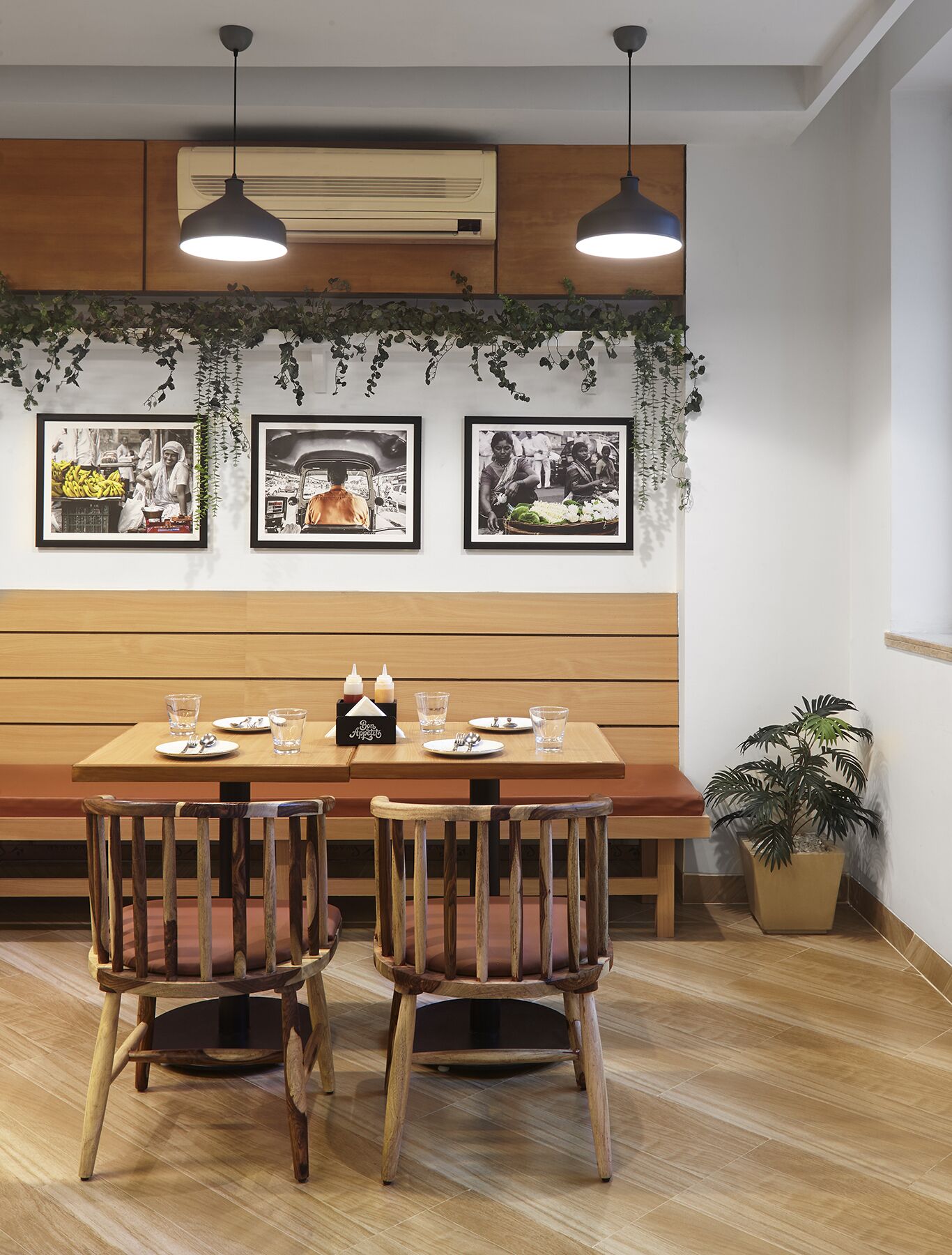 A dining area with a wooden table and chairs, framed pictures on the wall, and hanging plants.