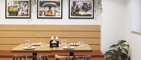 A dining area with a wooden table and chairs, framed pictures on the wall, and hanging plants.