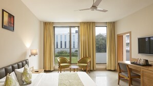 A hotel room with a bed, two chairs, a desk, a television, and large windows with curtains. - Monday Hotels Mahape (Navi Mumbai)