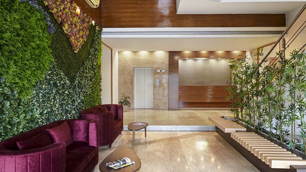 A modern lobby with a green wall, a red sofa, a wooden staircase, and a reception desk. - Monday Hotels Mahape (Navi Mumbai)