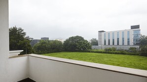 A balcony with a view of a grassy area and a modern building with large windows. - Monday Hotels Mahape (Navi Mumbai)