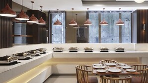 A modern kitchen with pendant lighting, a built-in stove, and a dining area with wooden chairs and a table set for four. - Monday Hotels Mahape (Navi Mumbai)