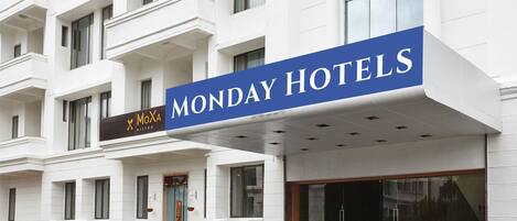 A hotel with a prominent "MONDAY HOTELS" sign, a MoXia Bistro, and a modern entrance with large windows.
