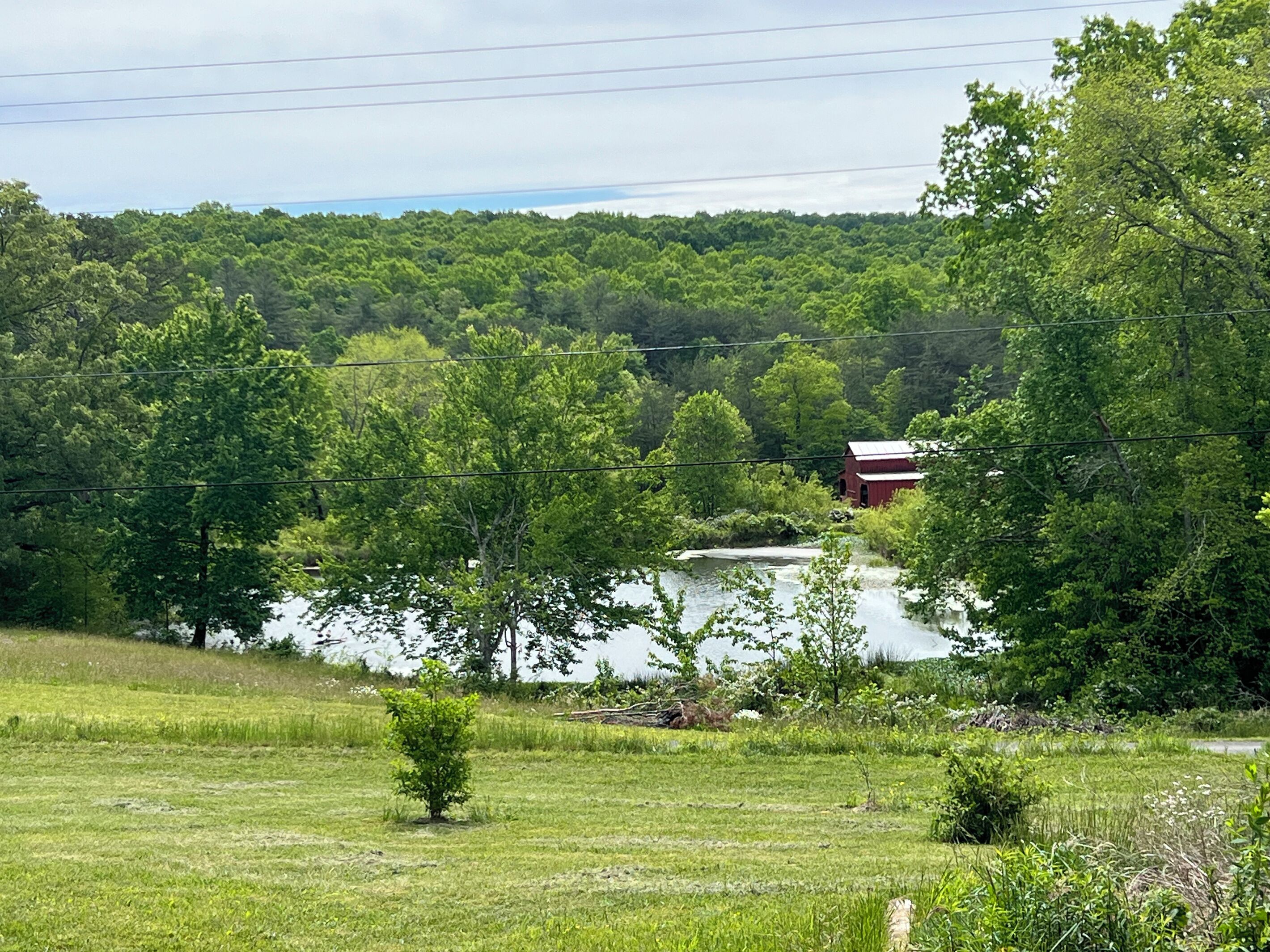 A rural landscape with a lake, trees, and a red barn.