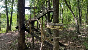 A wooden platform with a sign warning of risk, surrounded by trees. - Private East Tennessee Glamping Cabins in a Treehouse Campground Pet Friendly (Grandview)