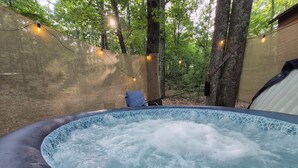 A hot tub surrounded by trees, with string lights and a chair. - Private East Tennessee Glamping Cabins in a Treehouse Campground Pet Friendly (Grandview)