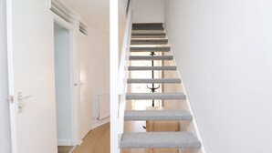 Eine Treppe mit grauen Teppichstufen und einem hölzernen Geländer, die zu einem Raum mit Heizkörper und Tür führt.