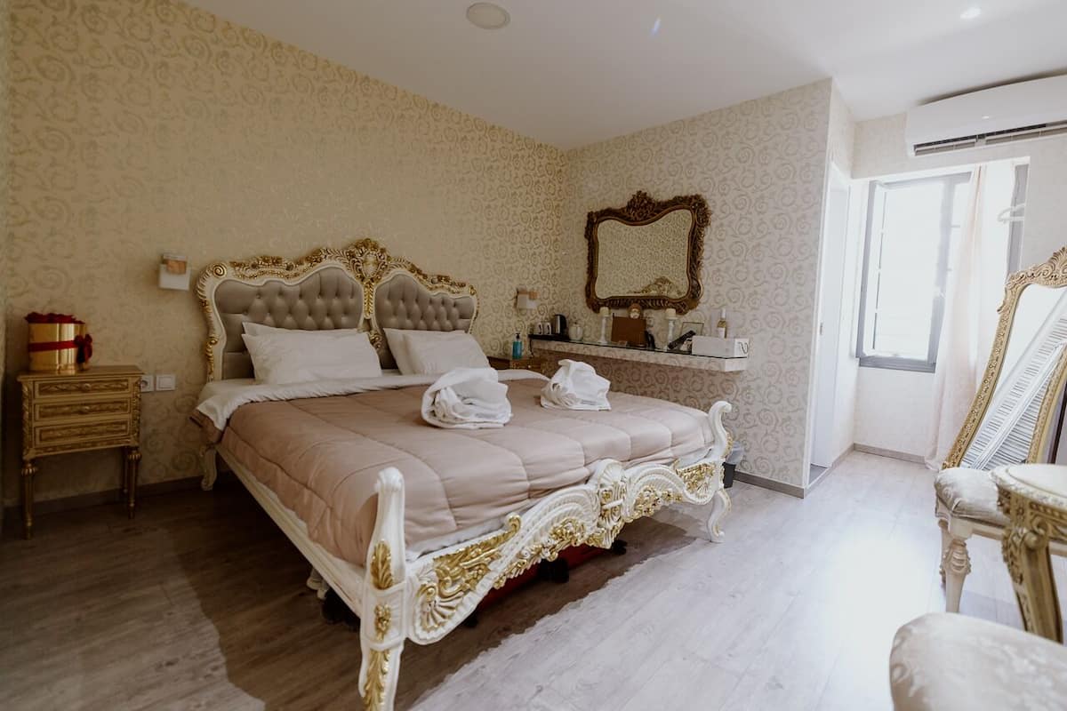 Un dormitorio amplio con una cama grande, muebles ornamentales y un espejo en la pared.
