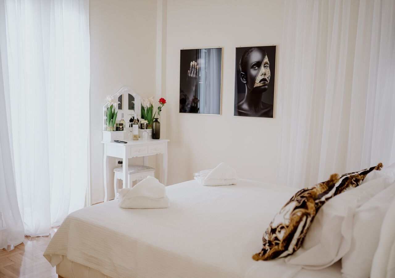 A hotel room with a bed, a desk, and two framed pictures on the wall.